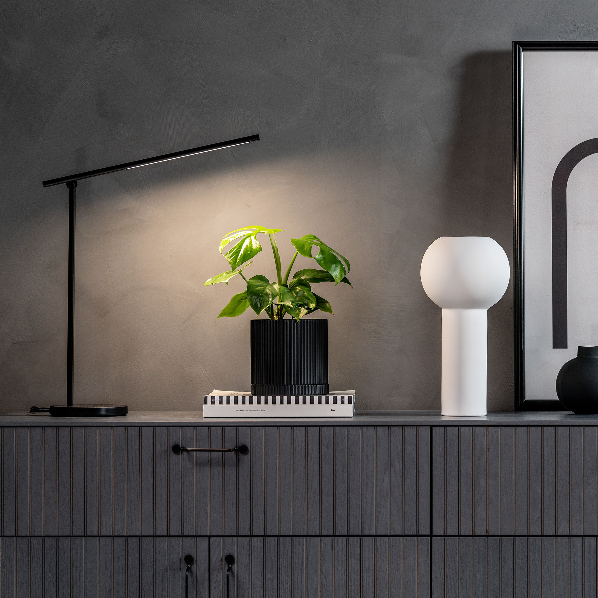 Minimalistische Schreibtischbeleuchtung mit Pflanzenakzent auf dunklem Sideboard