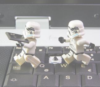 Zwei Stormtrooper-Figuren, die auf einer Laptop-Tastatur stehen. Einer hält ein Tablet in der Hand.