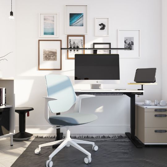 Ein modernes Büro mit einem Schreibtisch, einem Computer, einem Laptop, einem blauen Bürostuhl, einem Regal und mehreren gerahmten Bildern an der Wand.