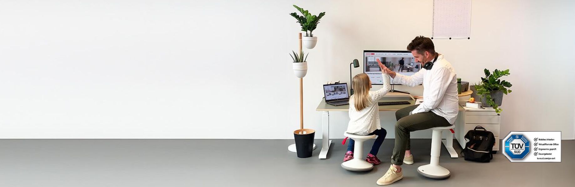 Ein Erwachsener und ein Kind sitzen an einem modernen Schreibtisch. Beide schauen auf einen Computerbildschirm, während sie interagieren. Es gibt Pflanzen im Raum und eine Tafel an der Wand.