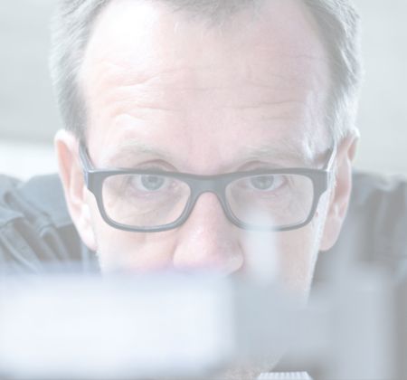 Nahaufnahme eines Mannes mit Brille, der fokussiert auf ein Objekt schaut.