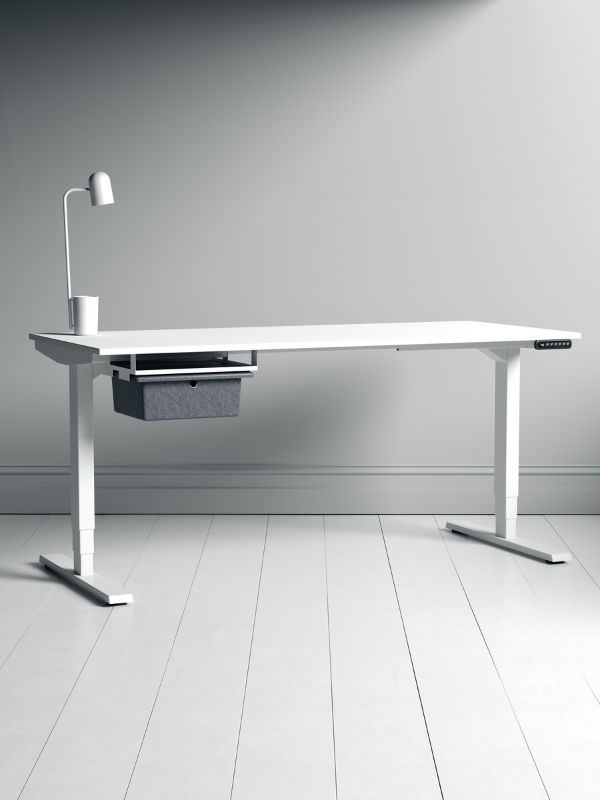 Schlichter weißer höhenverstellbarer Schreibtisch mit seitlicher Schublade und Lampe in minimalistischem Raum.