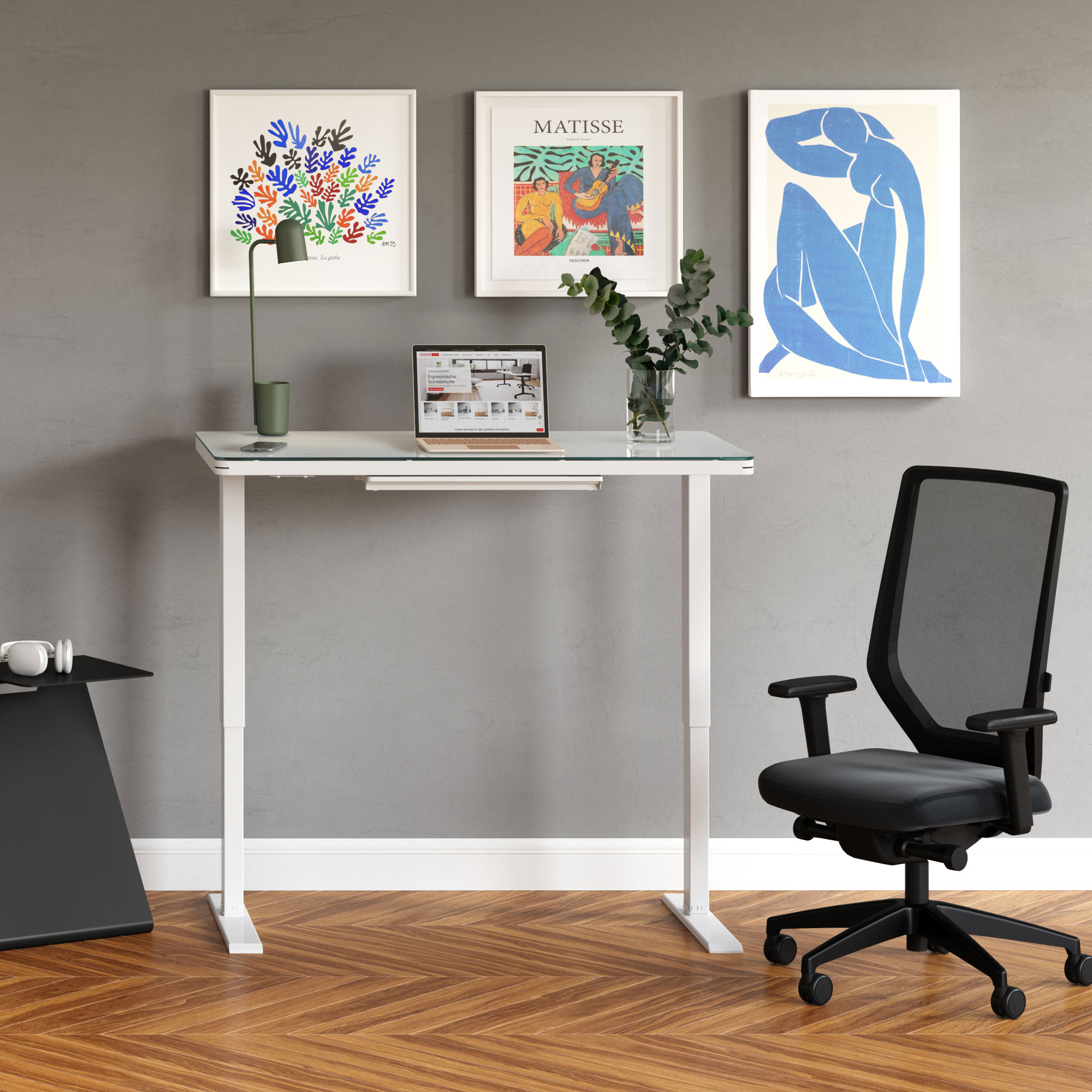 Ein moderner Arbeitsplatz mit einem Schreibtisch, einem Laptop, einer Nachttischlampe, Pflanzen und gerahmten Kunstwerken an der Wand. Daneben steht ein ergonomischer Bürostuhl.