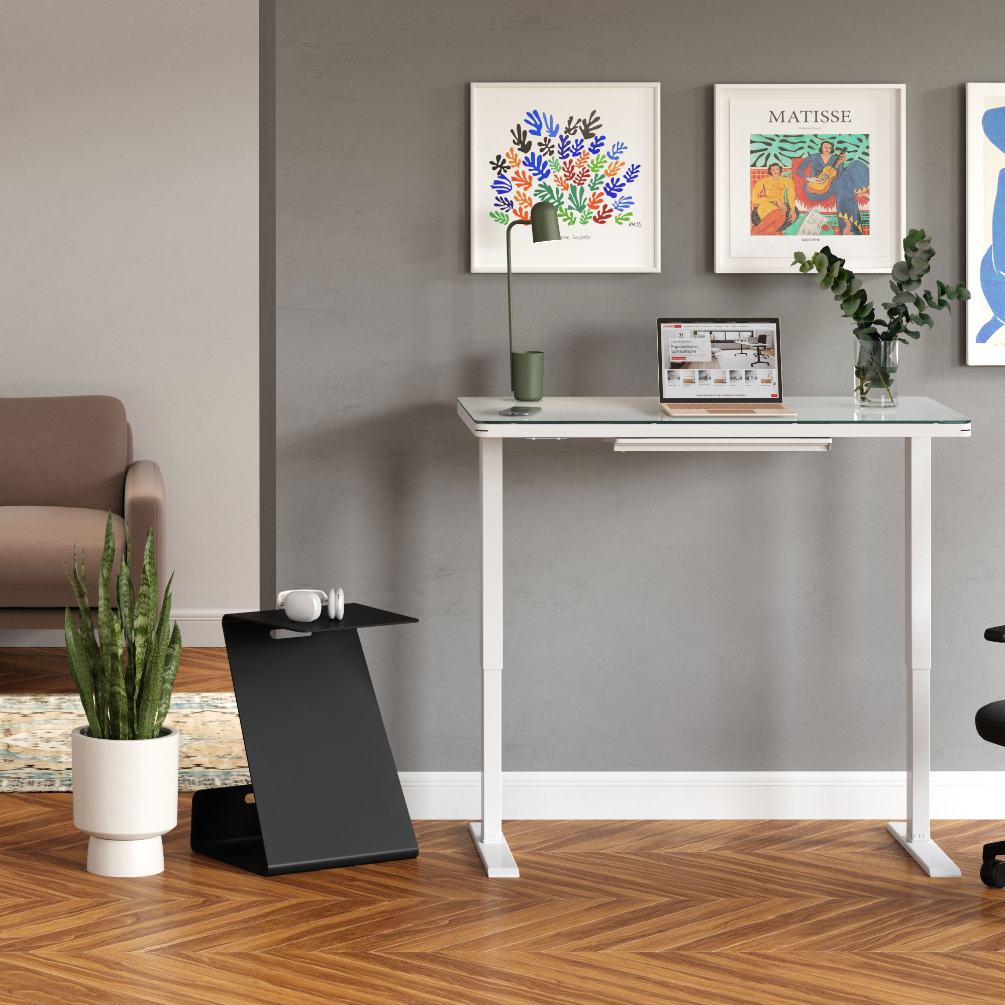 Ein moderner Arbeitsbereich mit einem höhenverstellbaren Schreibtisch, einer Lampe, einem Laptop, Pflanzen und Kunstwerken an der Wand.