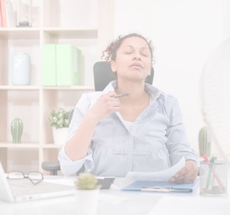 Eine Frau sitzt am Schreibtisch, hält Dokumente und scheint entspannt oder erleichtert zu sein. im Hintergrund sind Pflanzen und Büroartikel zu sehen.