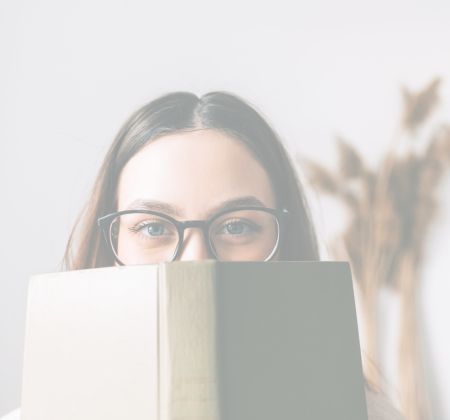 Frau mit Brille hält Buch vor Gesicht, Fokus auf den Augen