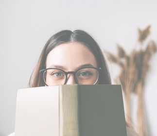 Eine Person mit Brille hält ein Buch vor ihrem Gesicht.